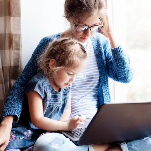 Working mom works from home office with kid. Mother and daughter read news. Woman and cute child